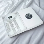 A premium white Cotton fabric men's panjabi neatly arranged inside a white gift box, featuring delicate white and silver embroidered design on the collar and both sides of the front placket with white round buttons; the box lid displays a black circular logo with the brand name "YESFashion", also visible on the label inside the collar, photographed on a white fabric background.