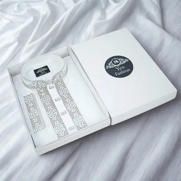 A premium white Cotton fabric men's panjabi neatly arranged inside a white gift box, featuring delicate white and silver embroidered design on the collar and both sides of the front placket with white round buttons; the box lid displays a black circular logo with the brand name "YESFashion", also visible on the label inside the collar, photographed on a white fabric background.